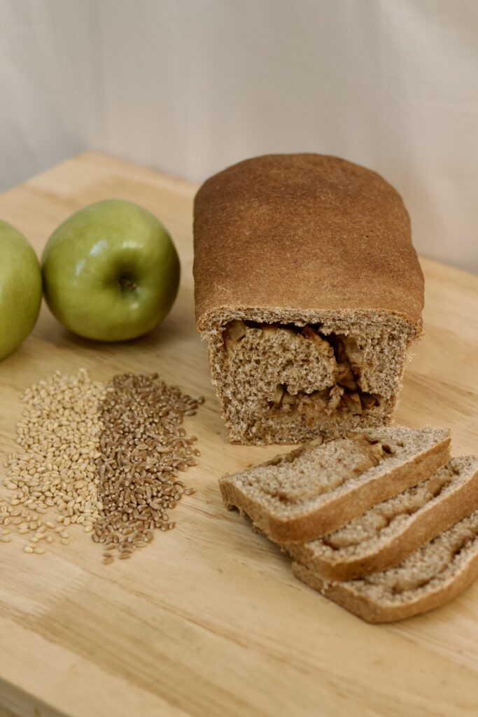 Photo of whole grain Abbot's apple bread, including organic green granny apples, organic soft white wheat berries, organic hard red heirloom wheat berries, and sliced loaf of Abbot's apple bread, made from organic ingredients.