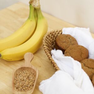 Photo of fresh bananas, wooden scoop of organic wheat berries, and cloth lined basket containing whole grain banana muffins made from organic ingredients.