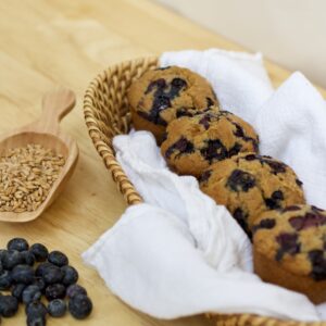 Photo of organic whole grain blueberry muffins with scoop of wheat berries and small assortment of blueberries.