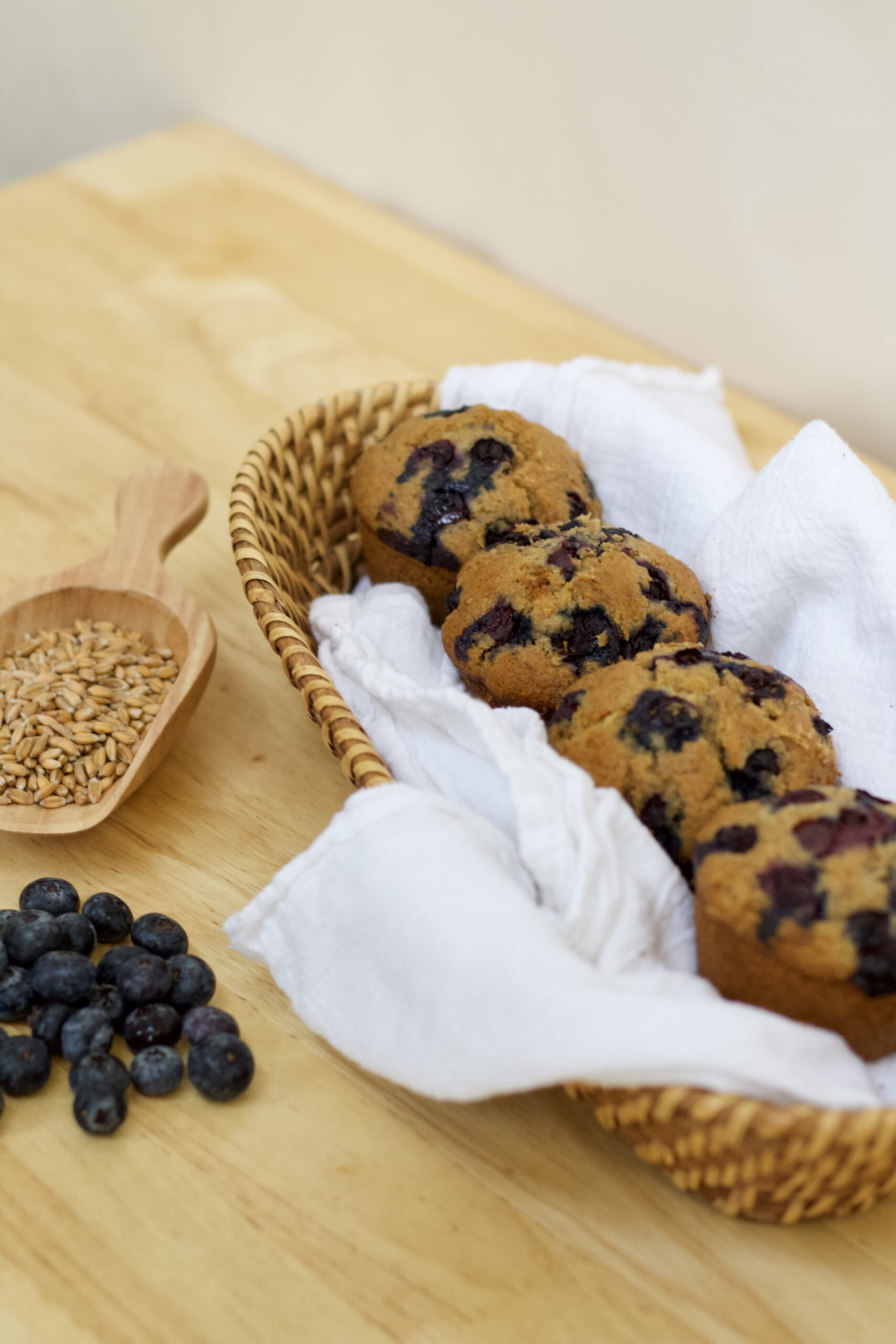 Photo of organic whole grain blueberry muffins with scoop of wheat berries and small assortment of blueberries.