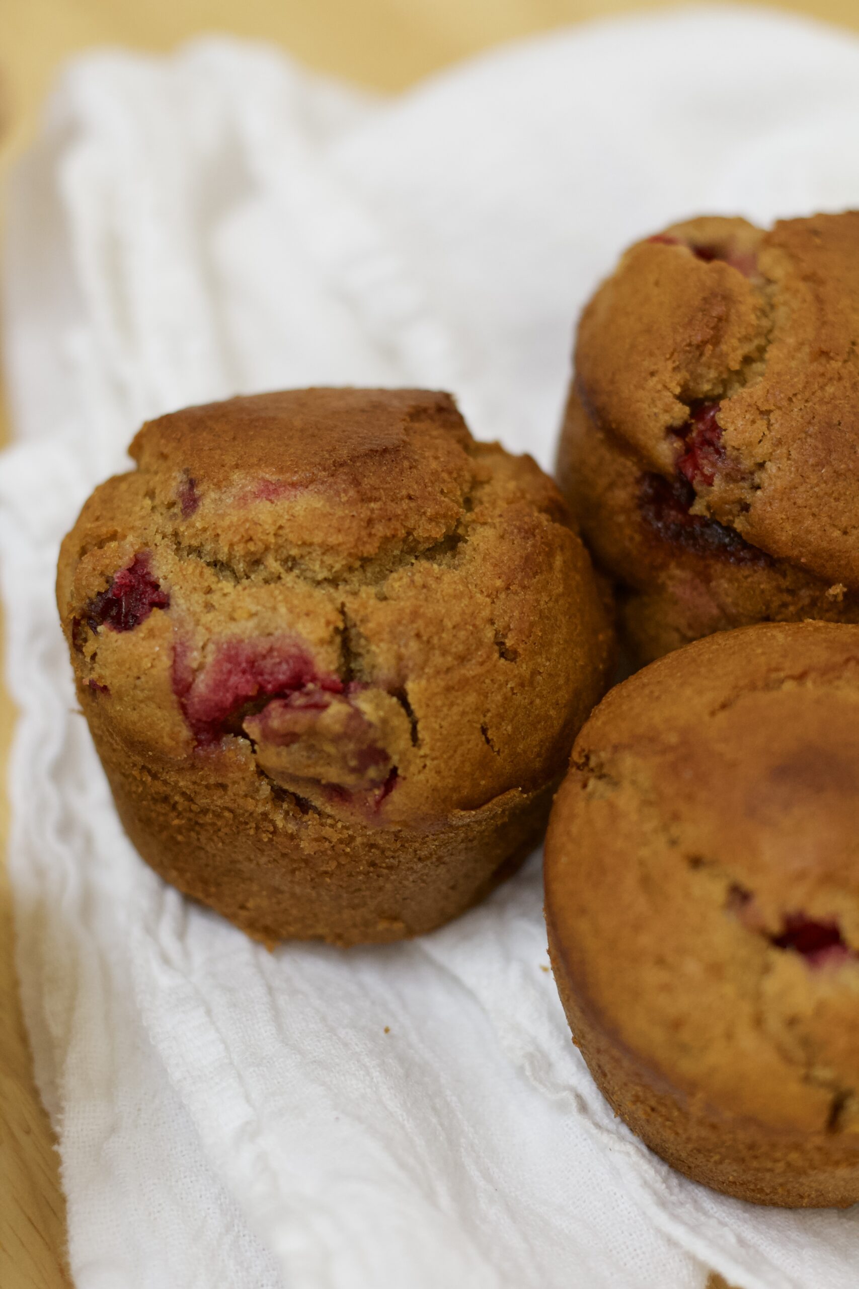 Close up photo of cranberry's glory whole grain muffins on a white cloth, made from organic ingredients.