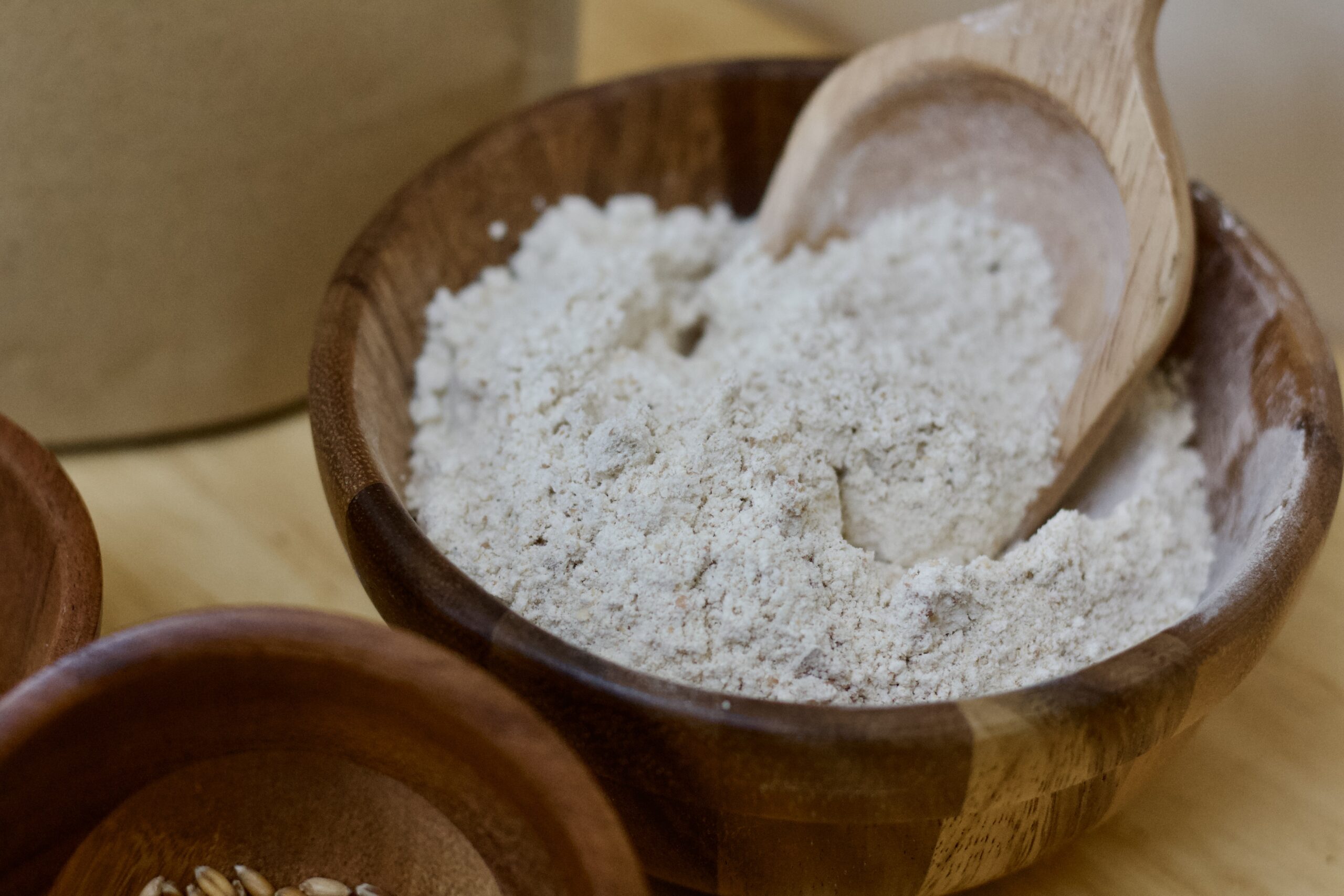 Close up photo of quickbread muffin whole grain flour in medium wooden bowl with wooden scoop.