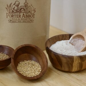 Photo of freshly milled whole grain white wheat flour blend, including sealable kraft flour bag, small wooden bowl of organic soft white wheat berries, small wooden bowl of organic hard white wheat berries, medium wooden bowl of freshly milled whole grain white wheat flour blend and small wooden scoop.