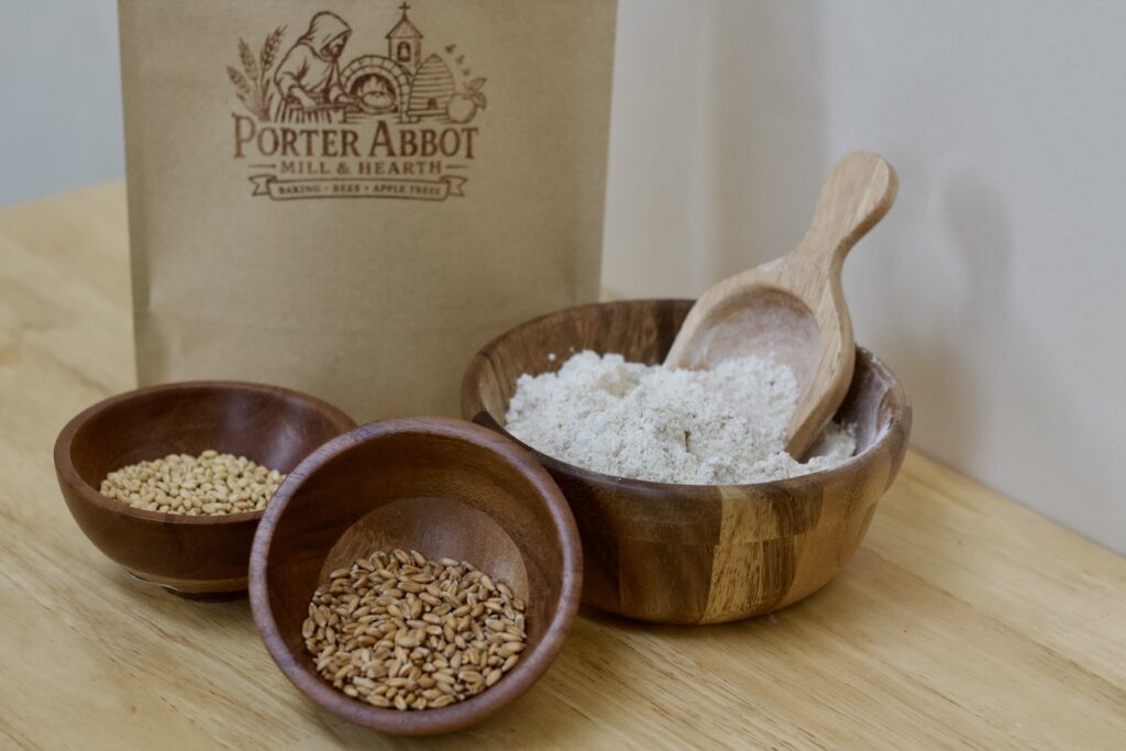 Photo of flour packaging, small wooden bowl of soft white wheat, small wooden bowl of spelt berries, and medium wooden bowl of quickbread muffin whole grain flour.