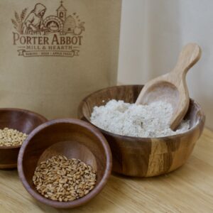 Photo of flour packaging, small wooden bowl of soft white wheat, small wooden bowl of spelt berries, and medium wooden bowl of quickbread muffin whole grain flour.